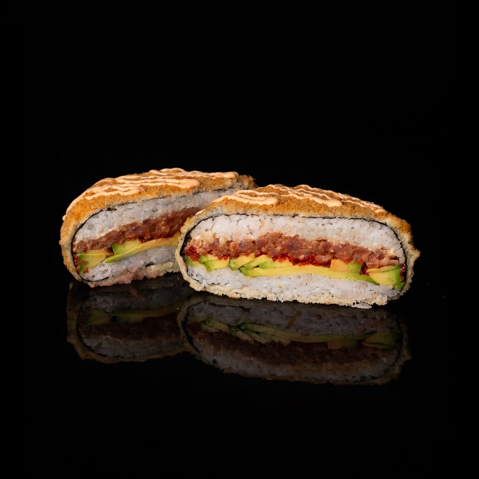 Two sushi rolls filled with tuna, avocado, and red tobiko, topped with crunchy breading and drizzled sauce.