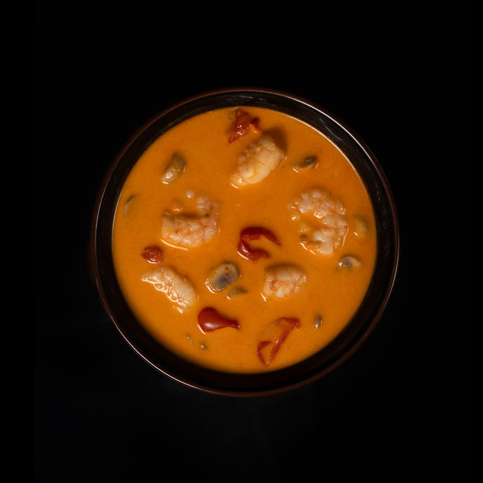 Bowl of shrimp in creamy orange curry sauce with mushrooms and red peppers on a black background.
